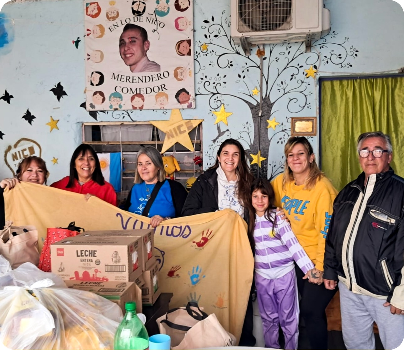 Vecinas y vecinos de Lo de Nico sosteniendo una manta pintada a mano junto a las donaciones recibidas